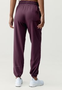 Burgundy joggerbyxor med en åtsittande elastisk midja, sidfickor och pucklade muddar. I kombination med vita sportskor. Slät textur.