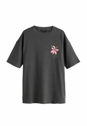 Dunkelgraues oversized T-Shirt mit kurzenärmeln, Rundhalsausschnitt und einer kleinen pinkfarbenen Blume mit grünen Blättern, die auf der linken Brust stickt ist.