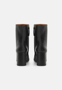 Botas de tobillo de cuero negro con punta cuadrada y un tacón grueso. Presentan un detalle de cremallera dorada en la parte posterior para el cierre.