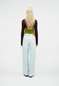 Μπλούζα μακρυμάνικη σε μπορντό και πράσινο, σε συνδυασμό με ανοιχτό μπλε τζιν με φαρδιά πόδια. Σημαντική λεπτομέρεια είναι μια εσωτερική ετικέτα με λογότυπο στην πίσω τσέπη.