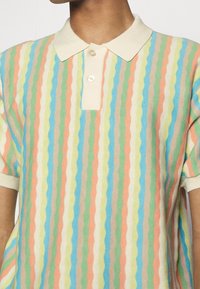 Stickad polo med färger i vågiga ränder: pastellorange, ljusgrön, blå och beige. Kort ärm och knäppbar krage.