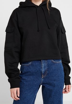 Haut cropped noir avec une texture côtelée, capuche à cordon de serrage et poches latérales. Assorti à un jean en denim bleu taille haute.