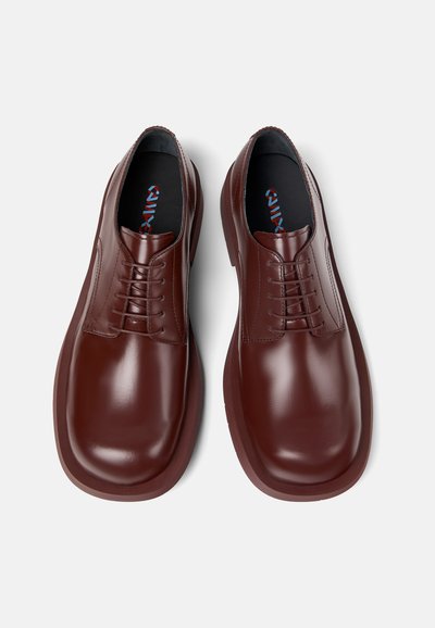 Scarpe in pelle marrone con una finitura liscia, punta tonda e design con lacci. Le solette nere presentano un marchio colorato. Suola in gomma leggera.