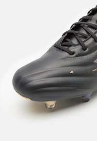 Scarpa da calcio nera con tomaia in materiale sintetico texturizzato, tacchetti moldati e dettagli dorati. Il design è elegante, con punta arrotondata e chiusura a lacci.
