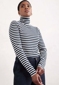 Garais piedurknēm, turtlenecks ar jūras zila un baltām svītrām, ribota tekstūra. Apvienots ar tumšiem džinsiem, ar redzamu pogu un jostas cilpām.