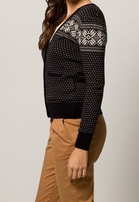 Svart kofta med vita geometriska mönster på axlarna, ribbade ärmmuddar och nederkant, åtsittande design och medelvikt stickad textur.