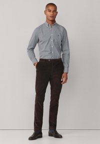 Camisa de cuadros azul claro con botones y mangas largas, combinada con pantalones de pana marrón oscuro. Se lleva con zapatos negros y calcetines con acentos azules.