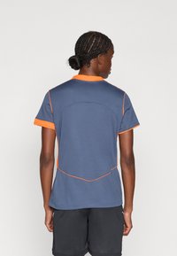 Sport t-shirt i mörkblått med orange detaljer. Har korta ärmar och en figursydd design med texturerad tyg och dekorativ sömnad.
