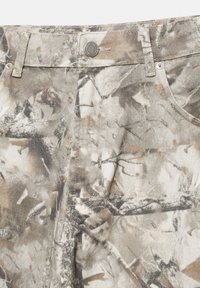 Textília s maskovacím vzorom so vzorom vetiev a listov, na ktorej sú zobrazené detaily ako kovový gombík v štýle denimu, pútka na opasok a stehy na prednom vrecku.