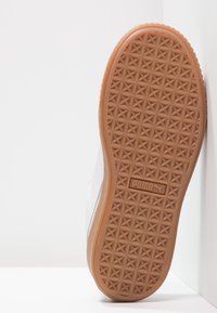 Zapatilla blanca con parte superior texturizada, suela de goma color caramelo con un patrón de diamantes y el logo de Puma. La suela muestra desgaste por uso.
