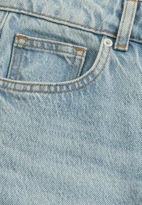 Tessuto di jeans azzurro chiaro con una piccola tasca frontale, caratterizzato da cuciture arancioni e un bottone a scatto in metallo sulla vita.
