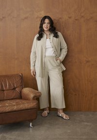 Svītrains, viegls auduma komplekts ar pogājamu kreklu un plašu bikšu kāju, pūdera bēša toņos. Izskatu papildina sandales ar plānām siksniņām.