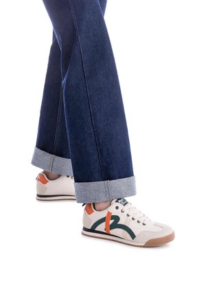 Zapatillas crema con detalles en verde y naranja, parte superior de textil, punta redonda, cordones y suela de goma, combinadas con unos pantalones de mezclilla oscuros y cortos.