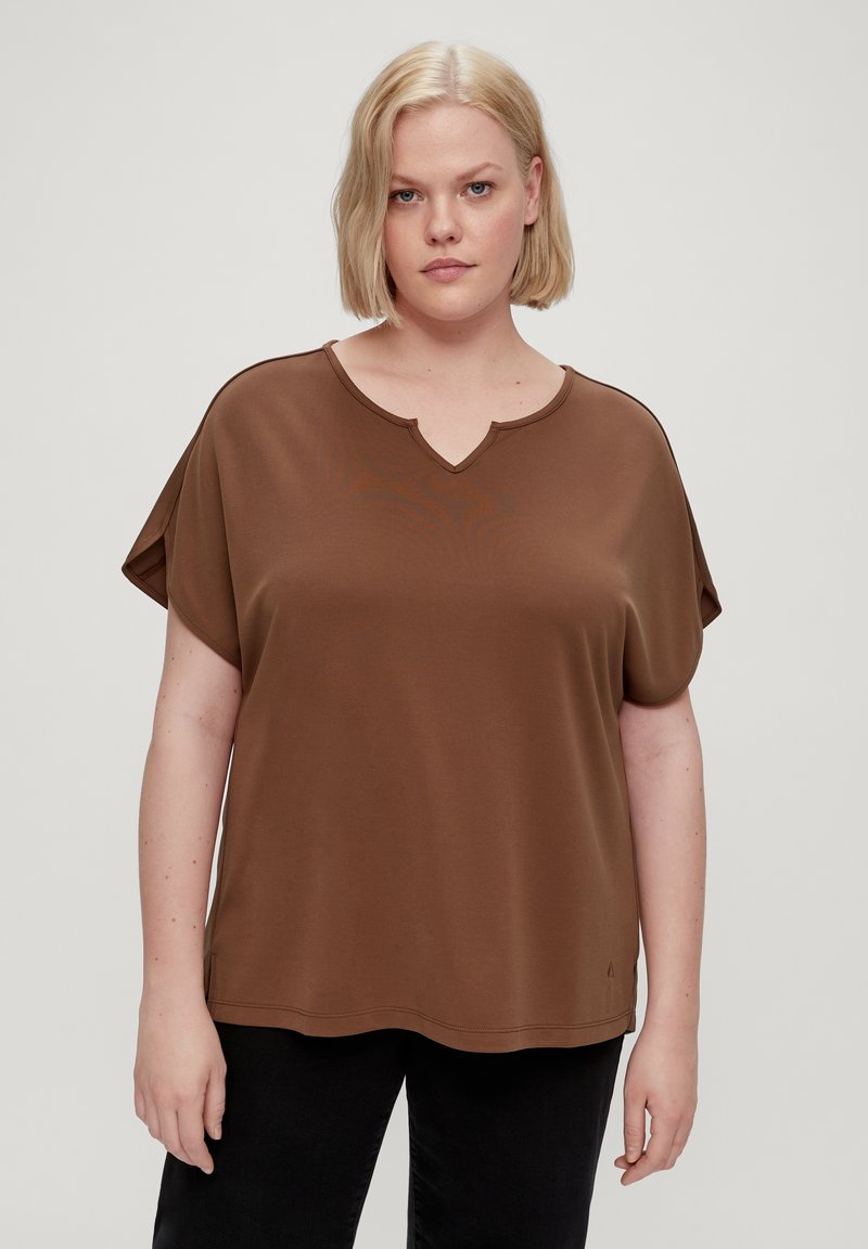 Top marrone a maniche corte con scollatura a V e vestibilità rilassata. Realizzato in tessuto morbido con una texture liscia. Dettagli di cucitura sobria ai bordi.