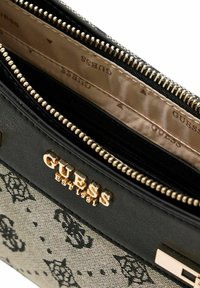 Portefeuille noir et beige avec un extérieur à motif, une quincaillerie dorée, un détail de logo, et deux compartiments zippés doublés d'un tissu clair.