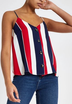 Mujer con top sin mangas con rayas verticales rojas, blancas y azules y botones negros en la parte delantera, combinado con vaqueros azules.