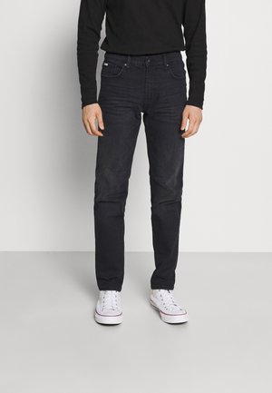 Czarne dżinsy o slim fit, z pięcioma kieszeniami i szlufkami na pasek, w połączeniu z białymi trampkami. Materiał ma gładką fakturę.
