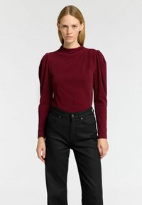 Burgunderfärgad långärmad topp med puffade axlar, texturerat tyg, hög halsringning; matchad med svarta höga jeans med enkel design.