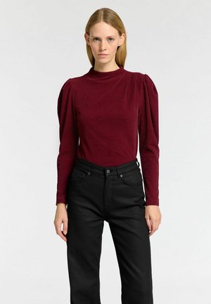 Burgunderfärgad långärmad topp med puffade axlar, texturerat tyg, hög halsringning; matchad med svarta höga jeans med enkel design.