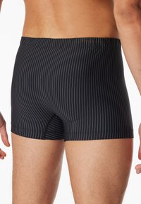 Boxer briefs a strisce nere con cintura elastica, caratterizzati da strisce verticali bianche, una texture liscia e una vestibilità aderente.