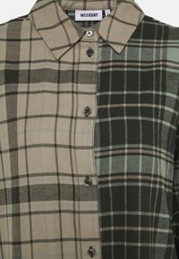 Chemise à motifs vichy mélangeant des teintes de beige, vert et noir, avec un boutonnage sur le devant et un col classique.