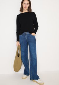 Maglione a coste neri, jeans a gamba larga blu, borsa tote beige e sneakers bianche con accenti chiari. Design semplice e vestibilità casual.