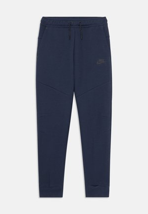 Tmavě modré zúžené teplákové kalhoty s elastickým pasem, černými šňůrkami, bočními kapsami a jemným logem Nike na pravém stehně.