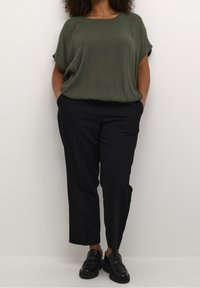 Olivenfarvet, løsstående bluse med rund halsudskæring, parret med sorte, skræddersyede bukser med lige snit og sidelommer.