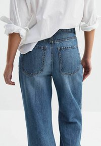 Jasnoniebieskie dżinsy o wysokim stanie, szerokiej nogawce, z delikatnymi przetarciami, dwoma tylnymi kieszeniami i postrzępionym dołem, w zestawie z białą, oversize'ową koszulą.