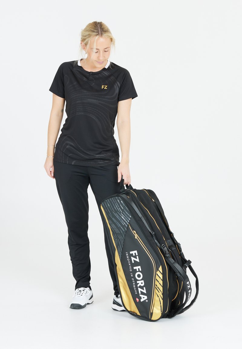 Musta urheilupaita, jossa on tekstuuripainatus, mustat housut ja suuri musta ja kultainen FZ Forza urheilulaukku, jossa on tyylikäs muotoilu ja useita osastoja.