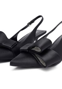 Des chaussures slingback en satin noir avec un embout pointu, ornées d'un grand nœud décoratif et d'accents en cristal au centre du nœud.