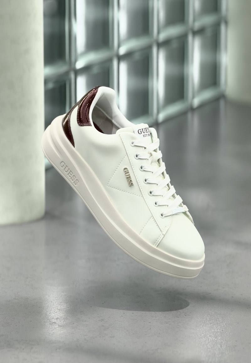 Witte leren sneaker met glanzende bordeauxrode accenten, ronde neus, vetersluiting aan de voorkant en een gestructureerde rubberen zool. Heeft het merkembleem aan de zijkant.