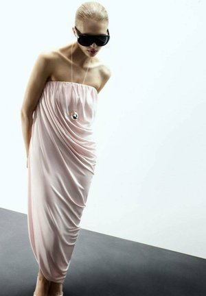 Abito rosa senza spalline realizzato in tessuto morbido, caratterizzato da un design drappeggiato. Il modello indossa occhiali da sole neri oversize e una collana circolare come accessorio.