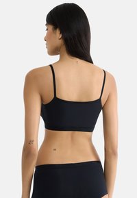 Černý bralet s tenkými ramínky, bezešvým designem, hladkým povrchem a širokým elastickým páskem; na pokožce pod oděvem se nacházejí tetování.