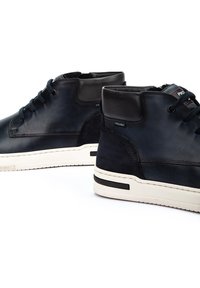 Zapatillas de deporte de caña alta en cuero y ante de color azul oscuro con cordones en la parte delantera, suela blanca en contraste y sutiles detalles de marca a los lados.