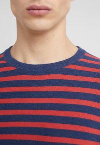 Blau-rot gestreifter Pullover mit Rundhalsausschnitt und gerippter Textur, der gleichmäßige horizontale Streifen über den Stoff zeigt.