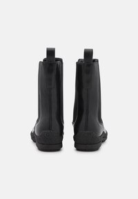 Botas de cuero negras hasta el tobillo con una superficie lisa, paneles laterales elásticos y suelas de goma texturizadas. Incluyen lengüetas para un fácil uso.