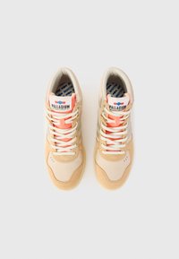 Des baskets montantes beiges en matériau textile et en suède. Les caractéristiques incluent des lacets orange, un col rembourré et le logo "PALLADIUM" sur la languette.