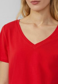 Czerwona, krótko rękawowa koszulka typu V-neck wykonana z miękkiej bawełny. Charakteryzuje się gładką teksturą oraz minimalistycznym designem z detalem wykończenia dekoltu.