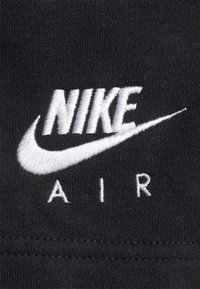 Vita broderad "NIKE"-text med swoosh-logotyp ovanför ordet "AIR" på svart stickat tyg.