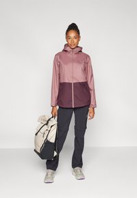 Water-resistant jacket with a light pink upper and dark burgundy lower section. Zippered pockets, hooded design, and sleek silhouette.