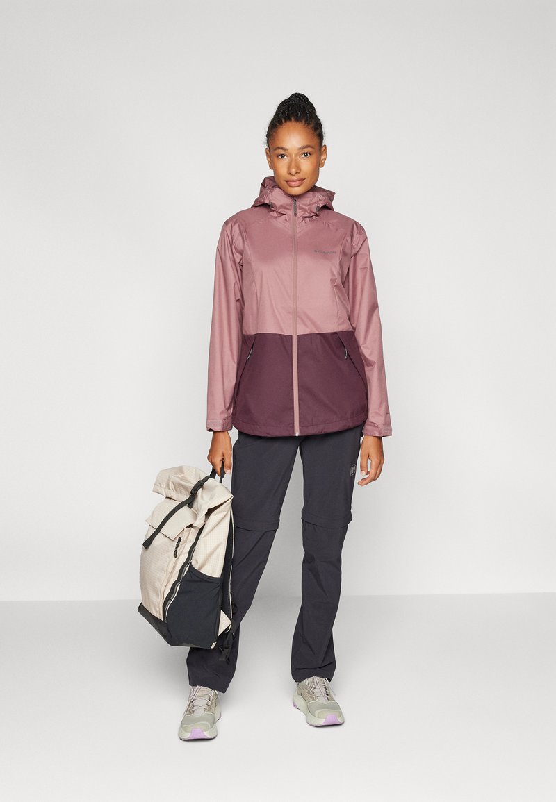 Veste résistante à l'eau avec une partie supérieure rose clair et une partie inférieure bourgogne foncé. Poches avec fermeture éclair, design à capuche et silhouette élégante.