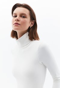 Langärmliges, rollkragenförmiges Oberteil in Weiß, figurbetontes Design mit glatter Textur. Mit hohem Kragen und dezenten Nahtdetails.