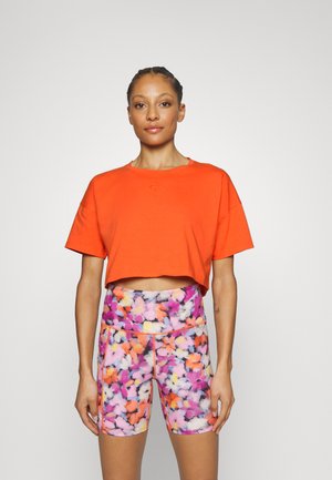 Orange cropped t-shirt with a round neckline paired with floral patterned shorts in pink, orange, and white, featuring a high waistband.