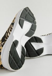 Baskets de sport à imprimé léopard avec une semelle intermédiaire texturée blanche et une semelle extérieure en caoutchouc noir présentant un motif de grip et un design structuré.