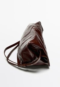 Brązowa skórzana torebka o błyszczącym wykończeniu, zwężanym kształcie i pojedynczym regulowanym pasku. Cechuje się subtelnymi przeszyciami i brakiem metalowych elementów.