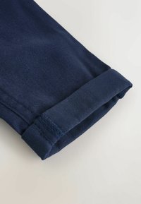 Nogawki z niebieskiego wielu materiału z podwiniętym mankietem. Gładka struktura i starannie wykonane szwy. Tkanina ma lekki połysk.