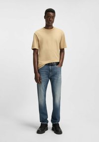 T-shirt beige a maniche corte con collo tondo, abbinata a jeans blu con un design sbiadito e scarpe nere con suole testurizzate.