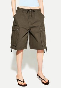 Olive green cargo shorts with a drawstring waist, side pockets, and adjustable hems, made from a lightweight fabric.