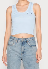 Světle modrý žebrovaný krátký top s kulatým výstřihem a nápisem "BDG JEANS". Kombinace s vysokým pasem a bledými modrými džíny.